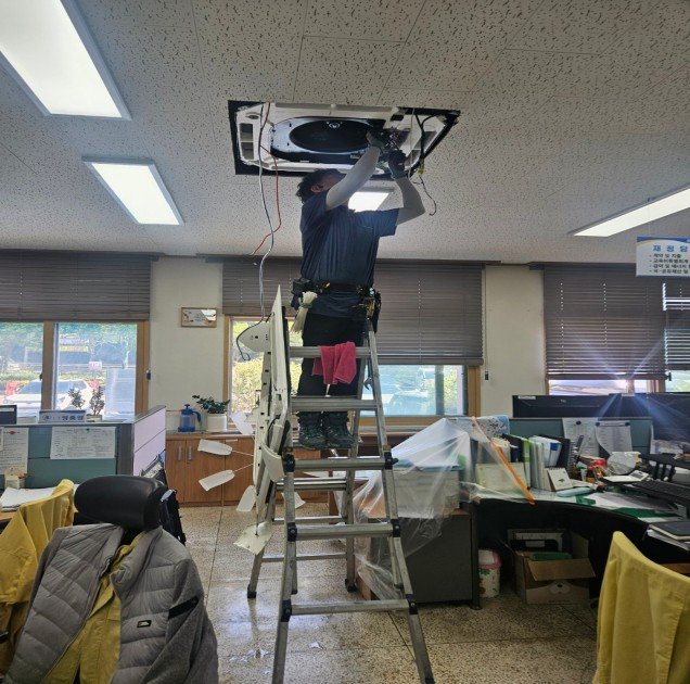 사다리에 올라 사무실 천장형 에어컨을 분해하는 작업자 뒷모습